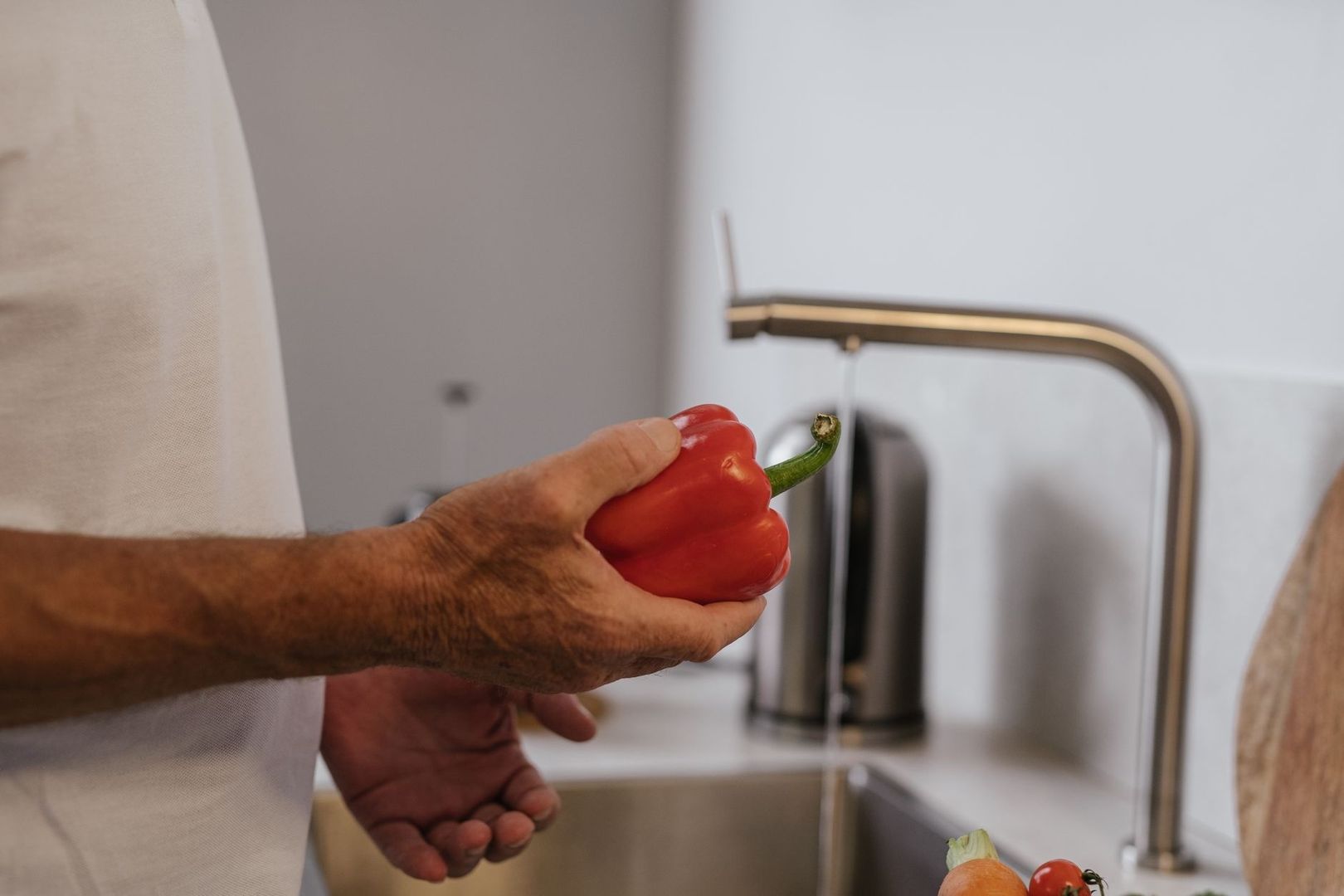 Hand håller en röd paprika vid kökskranen